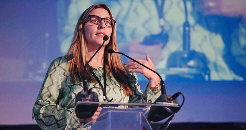 A woman stands at the lectern and gestures with her hands.